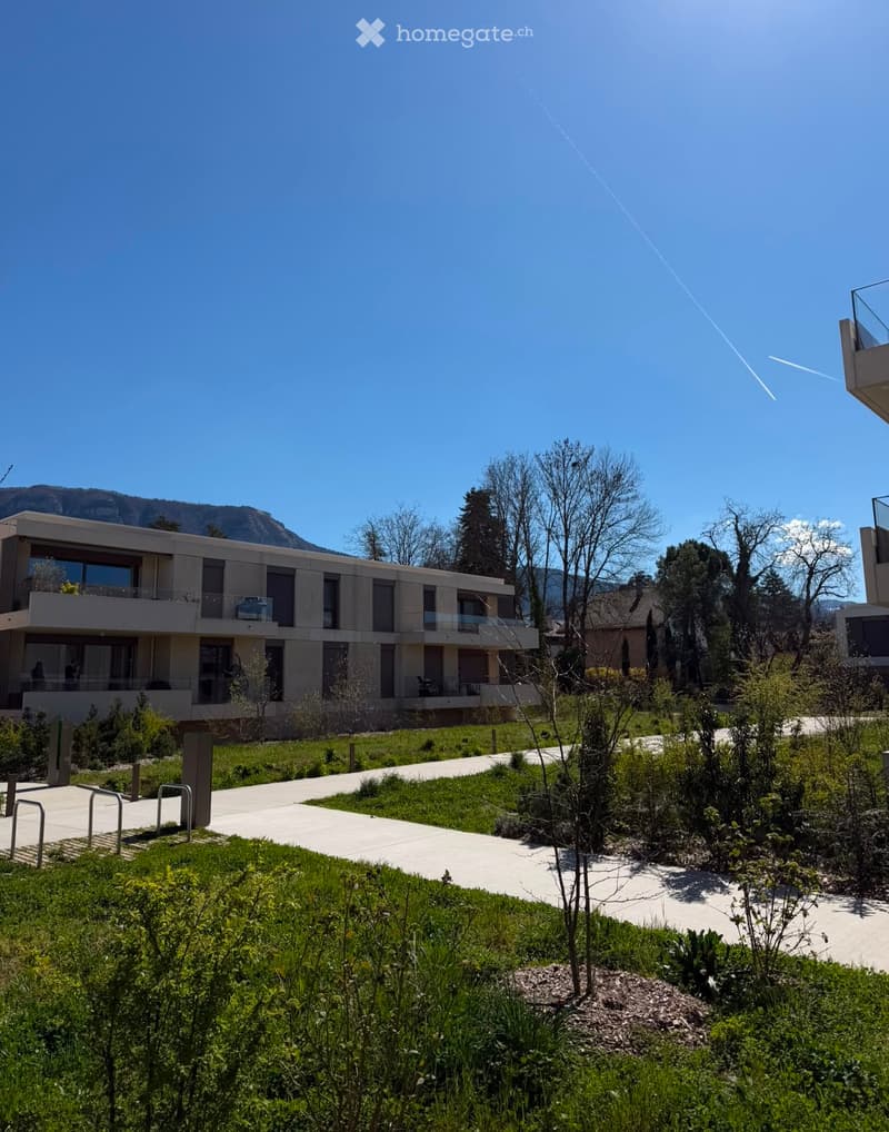 Modern residential building with large windows and balconies, surrounded by landscaped greenery and pathways.