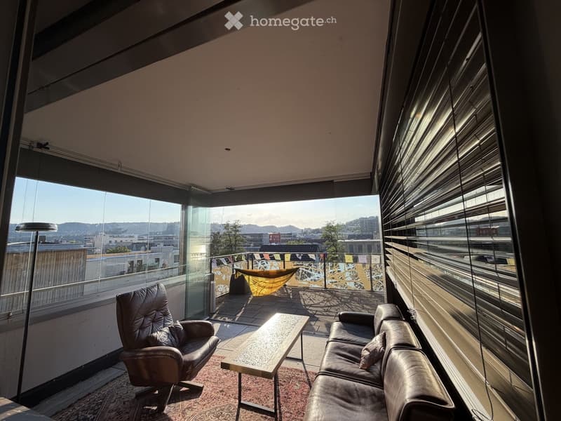 Modern living room with large windows offering a city view, featuring a leather sofa, coffee table, and armchair.