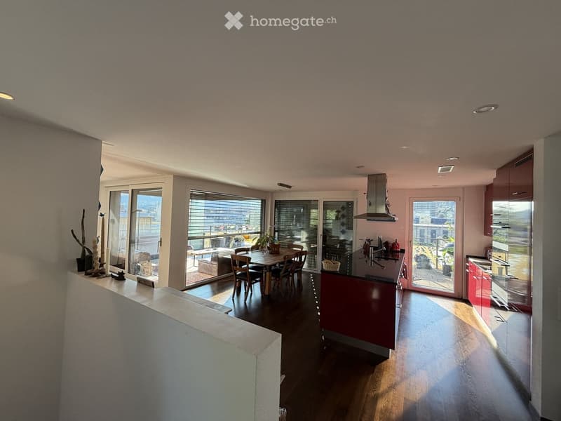 Modern open-plan kitchen and dining area with dark wooden floors, large windows, and a view of the city. Features a dining table with chairs, a kitchen island, and modern kitchen cabinets.