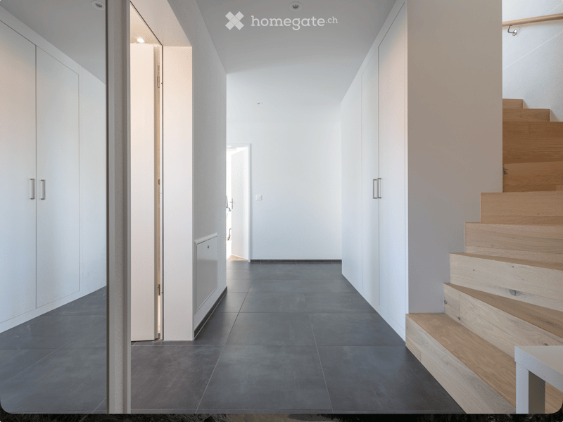 Modern hallway with dark tiled floor, white walls, built-in white cabinets, and a wooden staircase leading upwards.