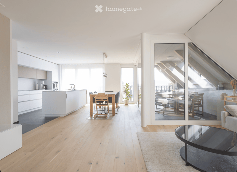 Open-plan living and dining area with light wood flooring, white kitchen cabinets, a dining table with chairs, a sofa, coffee table, and pendant lighting.