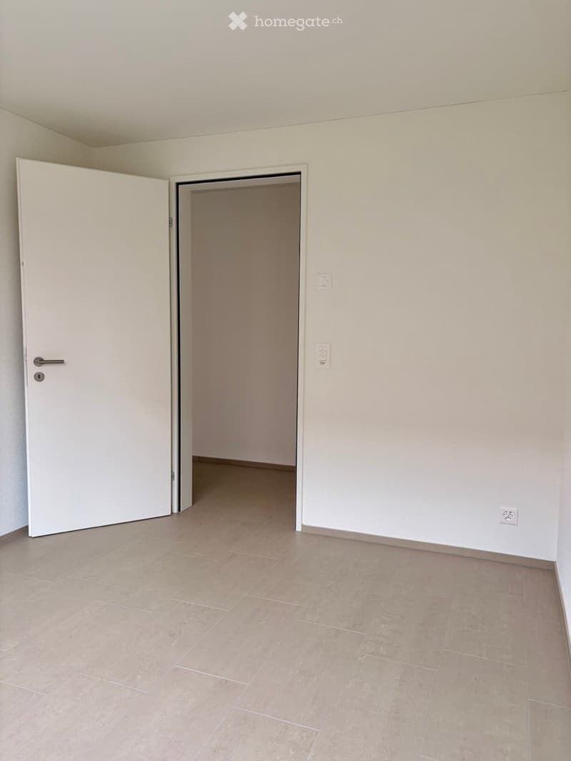 Empty room with beige tiled flooring, white walls, and two doors, one leading to another room.