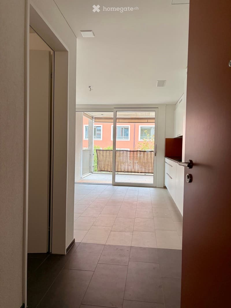 Empty hallway with tiled floor, white walls, and a sliding glass door leading to a patio area.