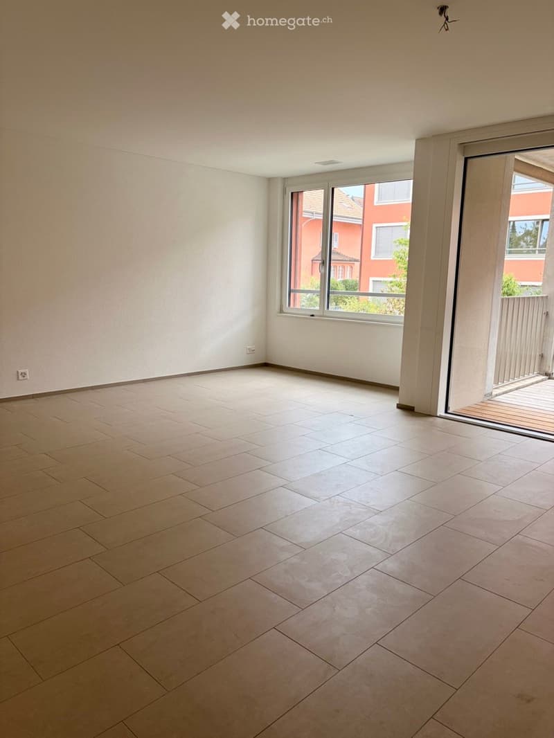 Empty room with light-colored tiled floor and white walls, featuring large windows and a sliding glass door leading to a balcony.