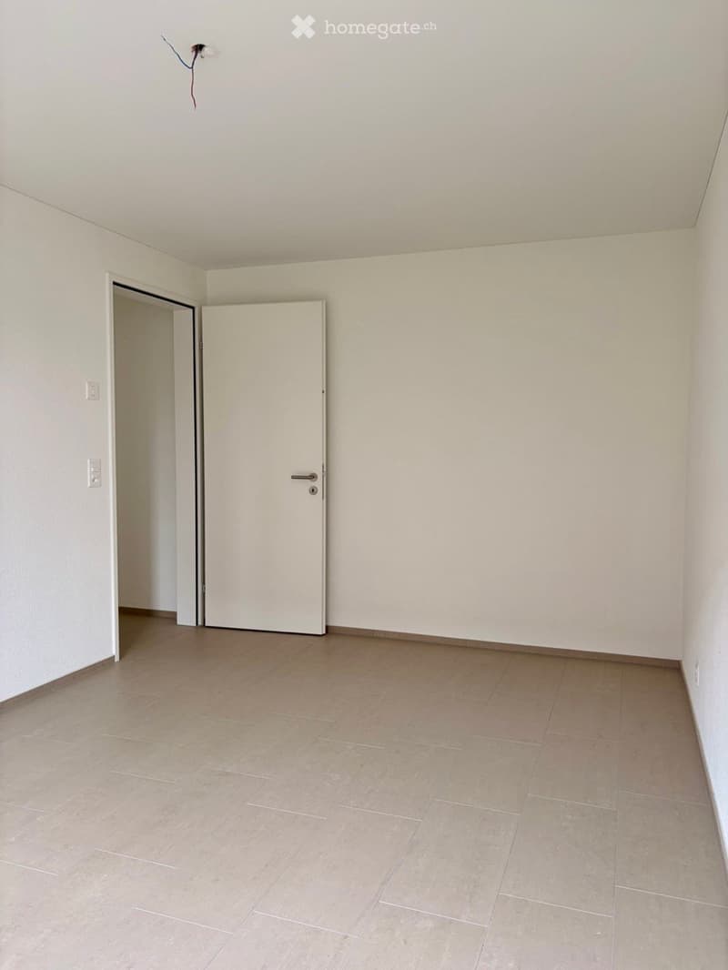 Empty room with light-colored tiled flooring and white walls, featuring a closed white door and an open doorway leading to another space.