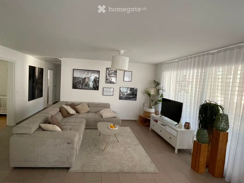 Modern living room with a large sectional sofa, coffee table, TV stand, side table, potted plants, and artwork on the walls.