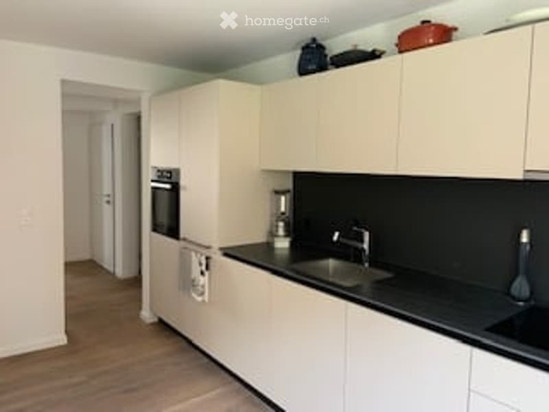 Modern kitchen with white cabinets, black countertops, and a stainless steel sink. Features include an oven, a blender, and a faucet.