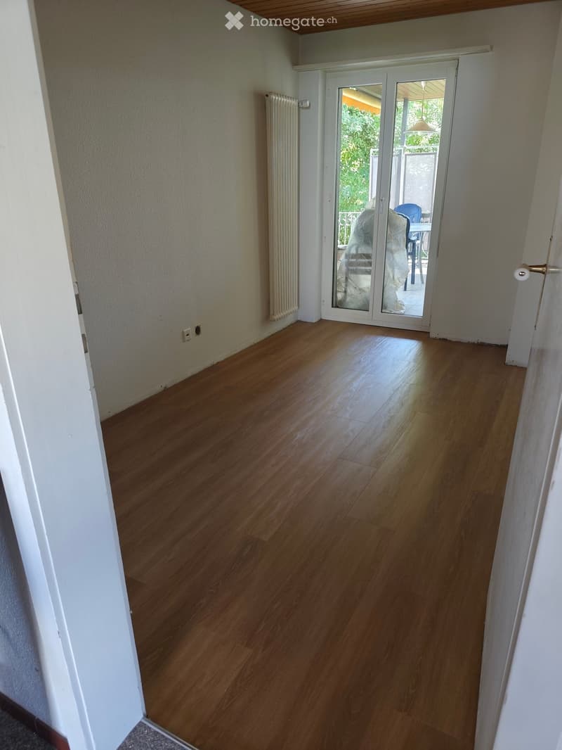 Empty hallway with wooden flooring, white walls, and a sliding glass door leading to an outdoor area.