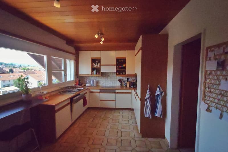 Bright kitchen with white cabinets, wooden countertops, and a tiled floor. Features a sink, dishwasher, and various kitchen appliances. A window offers a view of the surrounding area.