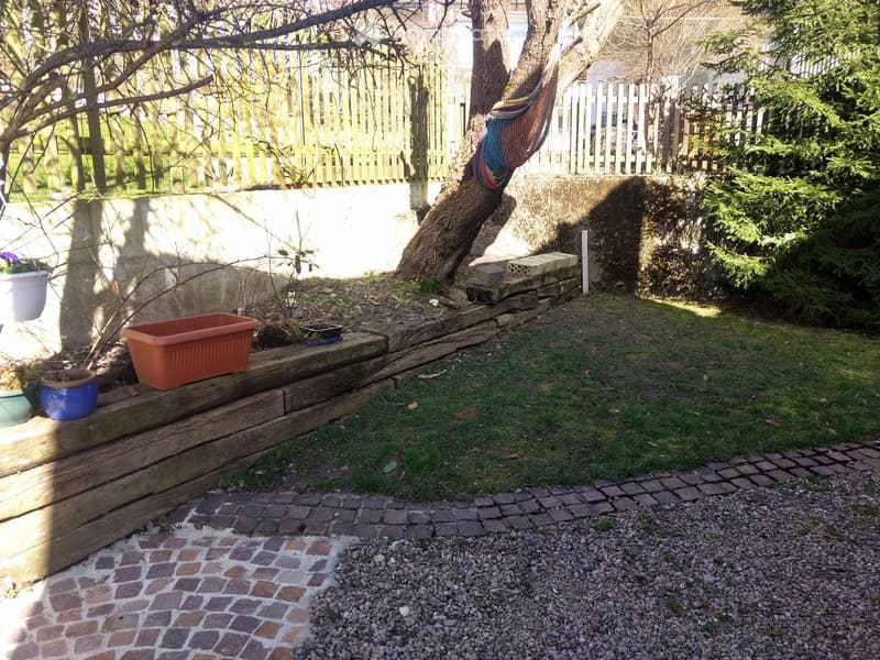 Garden with raised wooden steps, potted plants, a hammock, and a mix of gravel and brick pathways.