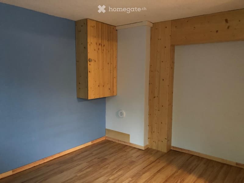 Empty room with wooden flooring, blue and white walls, and a small wooden cabinet mounted on the wall.