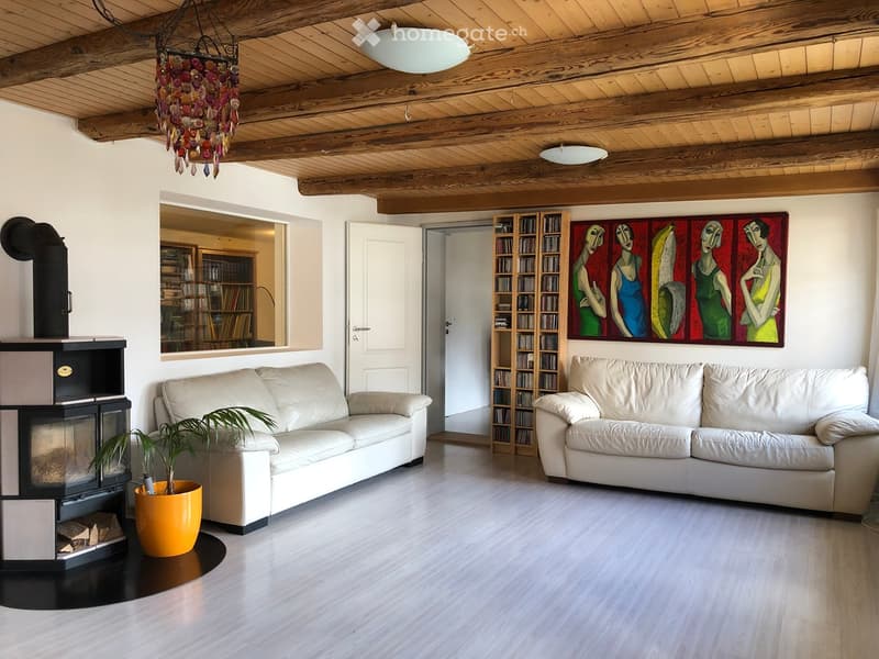 Bright living room with exposed wooden beams, two white sofas, a fireplace, a potted plant, and a colorful abstract painting on the wall.