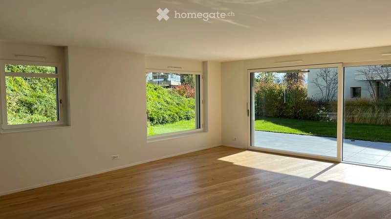 Empty room with wooden flooring, large windows, and sliding glass doors leading to a patio.