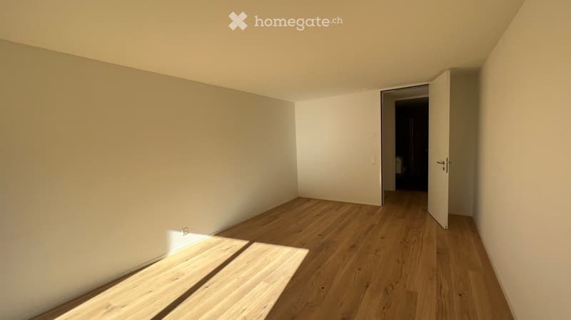 Empty room with light wooden flooring and white walls, featuring an open doorway leading to another space.