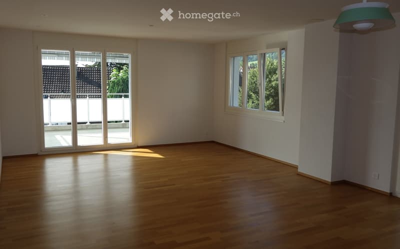 Empty room with wooden flooring, large windows, and sliding glass doors leading to a balcony.