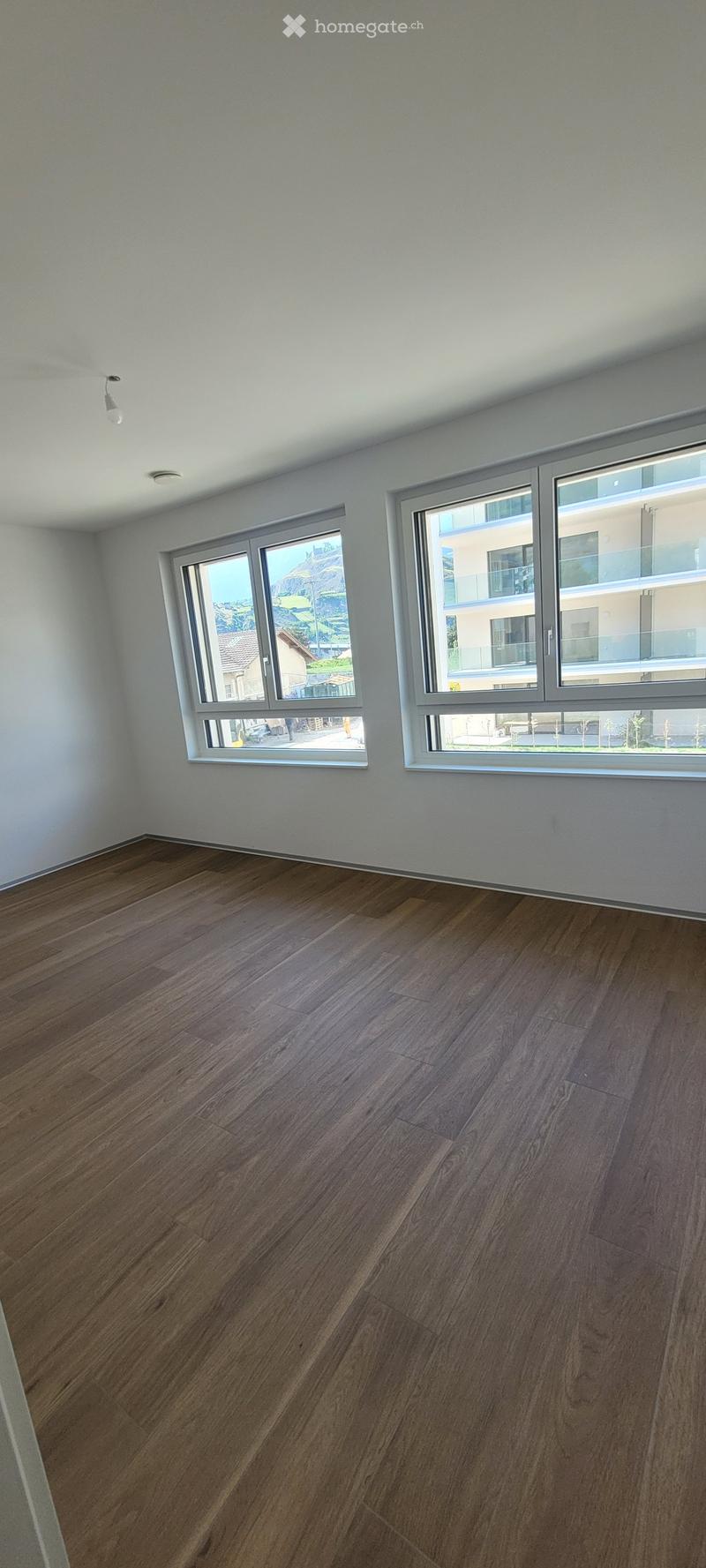 Empty room with wooden flooring and large windows offering a view of the outside area.