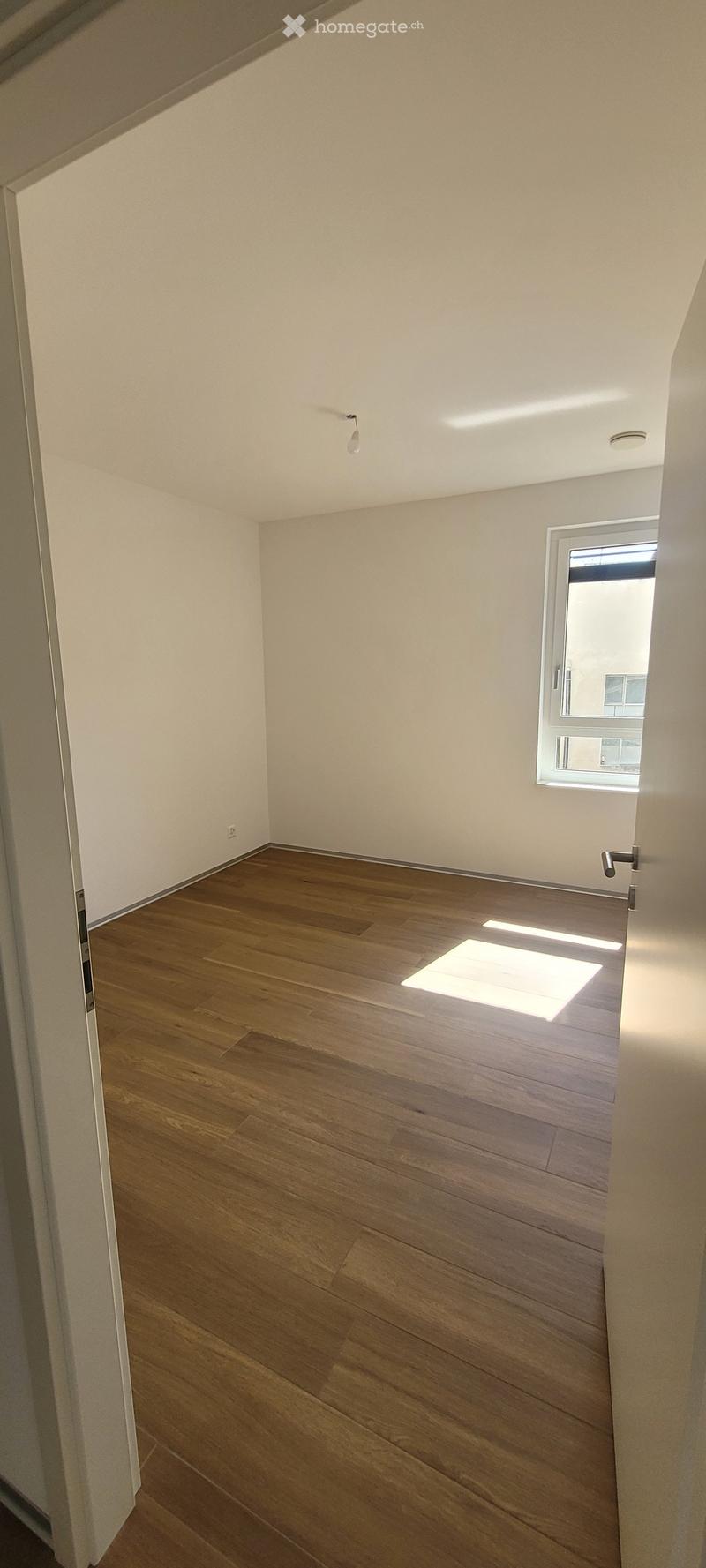 Empty room with wooden flooring, white walls, and a window letting in natural light. No furniture or equipment is present.