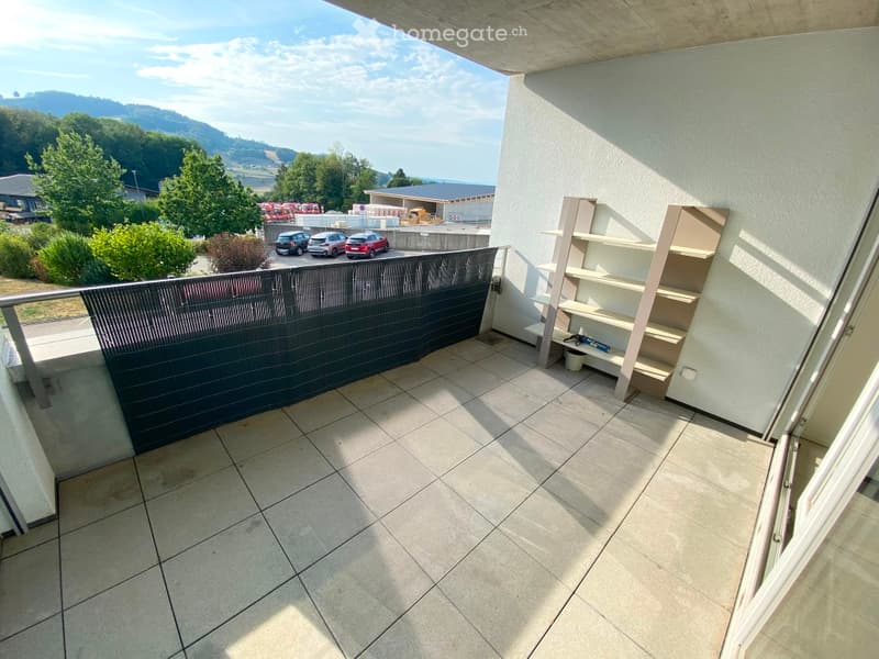 Balcony with tiled floor, metal railing, and a view of the surrounding area. A wooden shelf is placed against the wall.