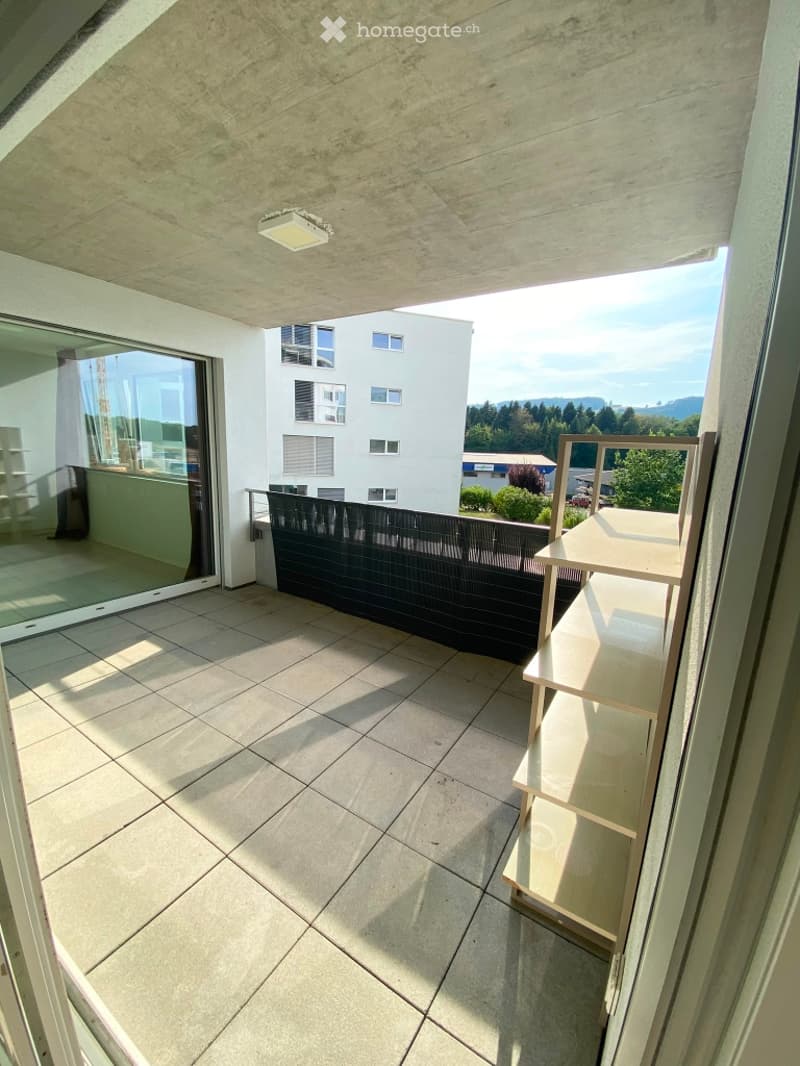 Balcony with tiled floor, modern railing, and a view of surrounding buildings and greenery.