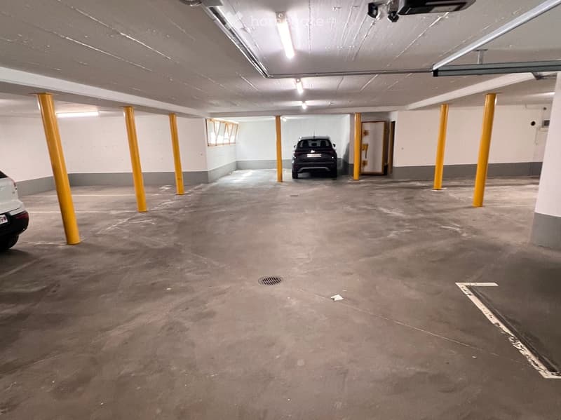 Underground parking area with concrete floor, yellow support pillars, and two parked cars.