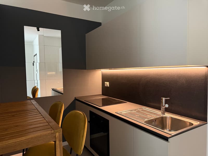 Modern kitchen with sleek white cabinets, a stainless steel sink, a built-in stove, and a wooden dining table with yellow chairs.