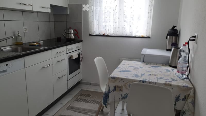Modern kitchen with white cabinets, black countertops, sink, oven, dishwasher, and a small dining area with a table and chairs.