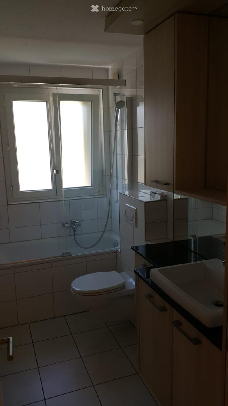 Modern bathroom with white tiles, a toilet, a sink, a shower, and built-in cabinets.