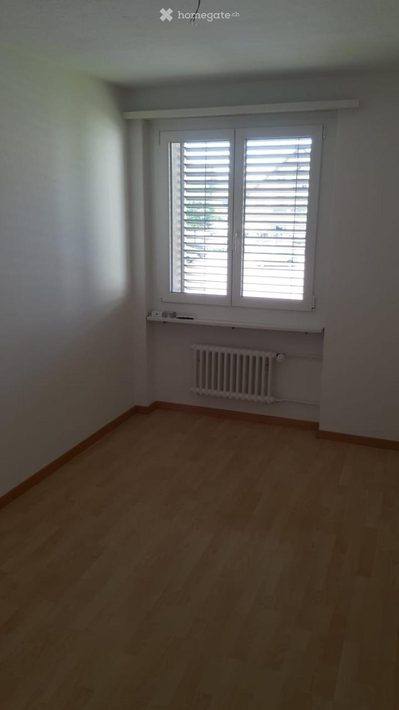 Empty room with wooden flooring, white walls, a window with blinds, a radiator, and a small shelf above it.