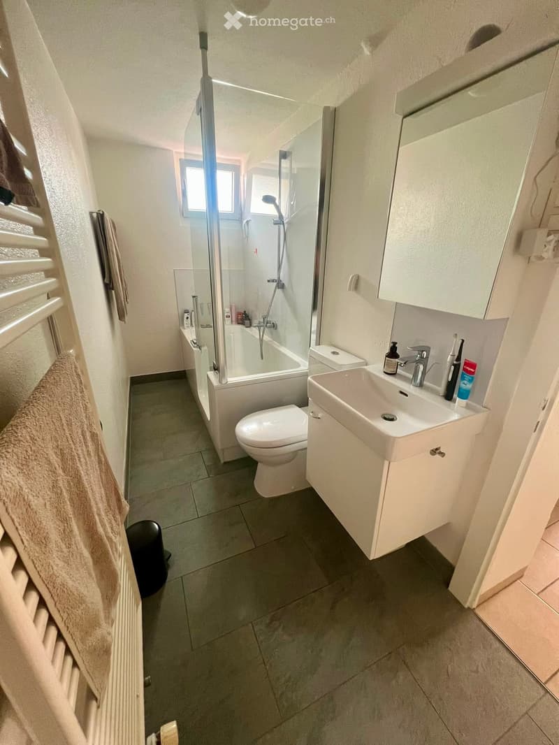 Modern bathroom with a white tiled floor, a toilet, a sink with a faucet, a shower, a mirror, and a towel on a radiator.