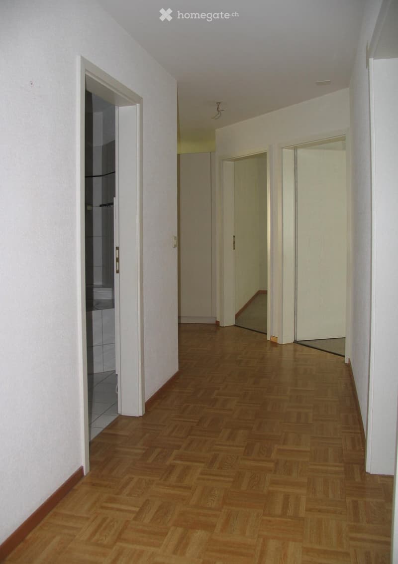 Empty hallway with wooden flooring, white walls, and several doors leading to other rooms.