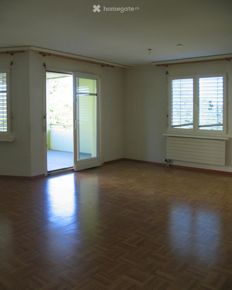 Empty room with wooden flooring, large windows, and a sliding glass door leading to a balcony.