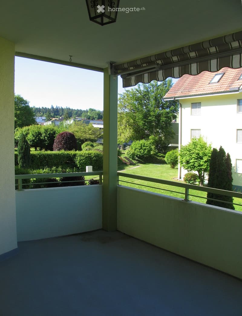 Balcony with a view of a well-maintained garden, featuring a railing, a retractable awning, and a lantern-style light fixture.