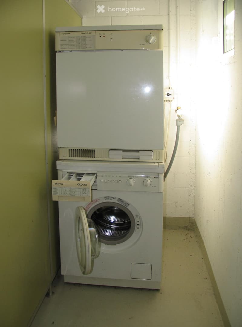 A small bathroom with a stacked washing machine and dryer unit against a white brick wall.
