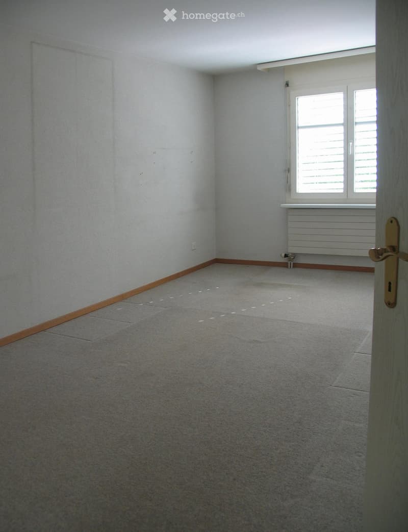 Empty room with light grey carpet, white walls, and a window with blinds. No furniture or equipment is present.