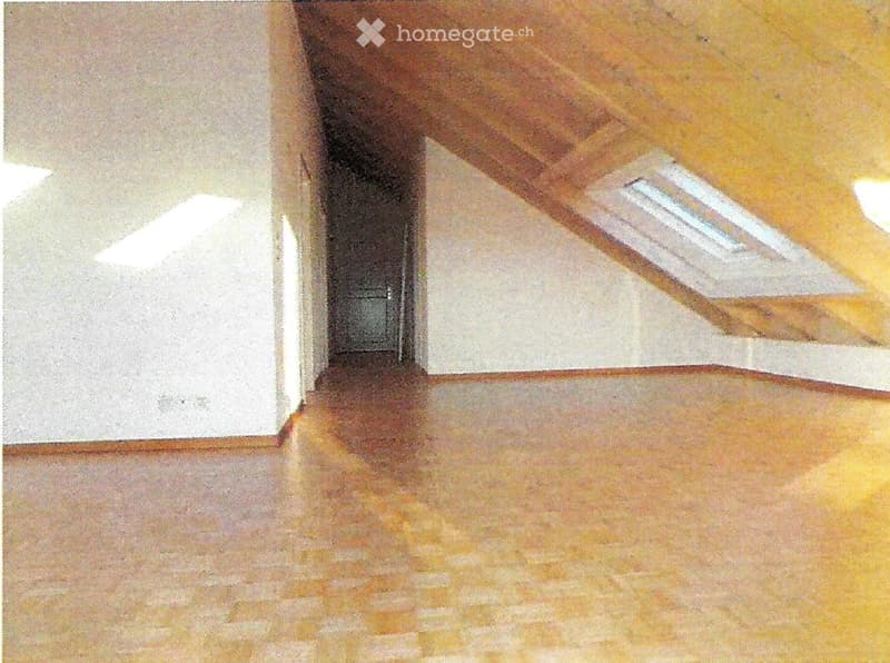 Empty room with wooden flooring and white walls, featuring a visible ceiling beam and a small window at the far end.