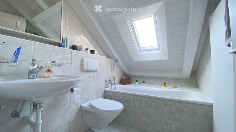 Cozy attic bathroom with skylight, white tiled walls, sink, toilet, bathtub, and small decorative items.