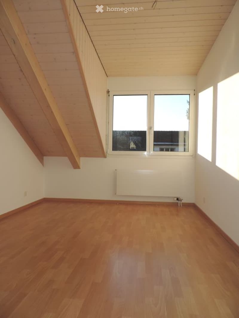 Empty attic room with wooden floors, white walls, and large windows, featuring exposed wooden beams on the ceiling.