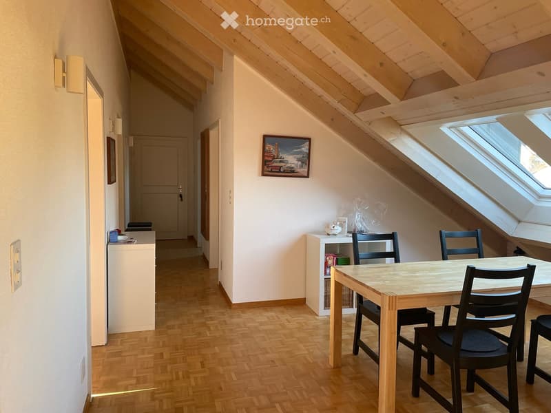 Bright attic room with wooden floors, slanted wooden ceiling, skylights, and a small dining area with a table and chairs.