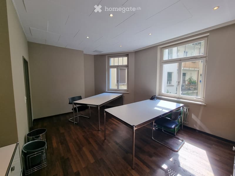Bright room with wooden flooring, two tables, chairs, and trash bins near the wall.