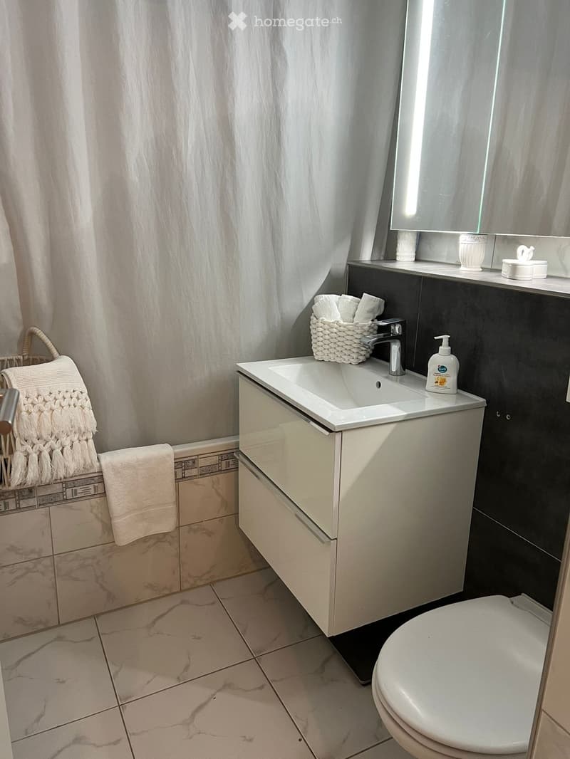 Modern bathroom with a white sink, chrome faucet, marble tiles, and a neatly arranged towel and basket on the side.