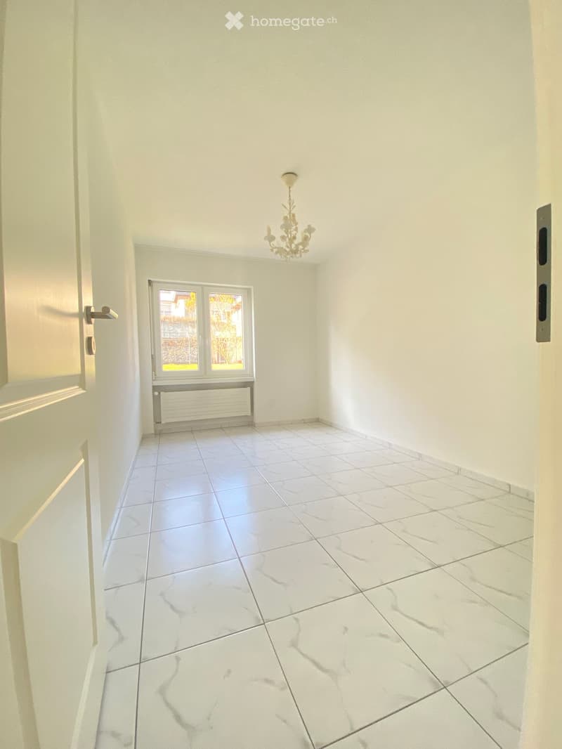 Empty room with white walls, marble tiled floor, a window with a radiator below, and a chandelier hanging from the ceiling.