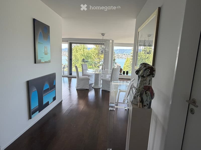 Modern dining area with hardwood floors, large windows offering a scenic view, a glass dining table with white chairs, a large mirror, and a decorative sculpture.
