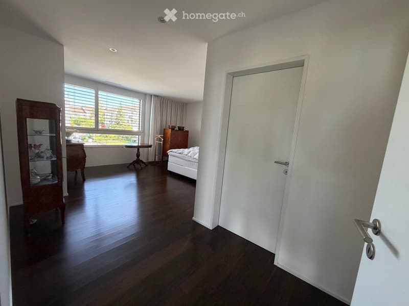Bright bedroom with wooden flooring, large window with blinds, bed, small table, cabinet, and mirror cabinet.