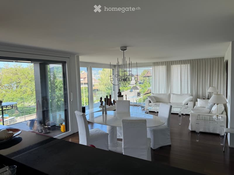 Modern living and dining area with white furniture, large windows, and a chandelier.