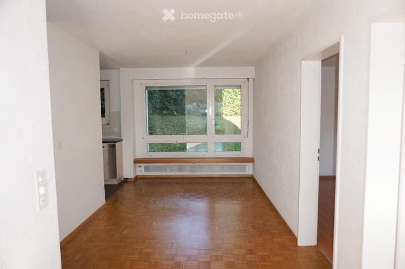 Completely empty room with wooden flooring, white walls, large windows, and a bench beneath the windows.