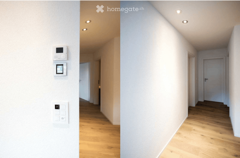 Empty white hallway with wooden floors and recessed lighting, entrance door, control panel with thermostat