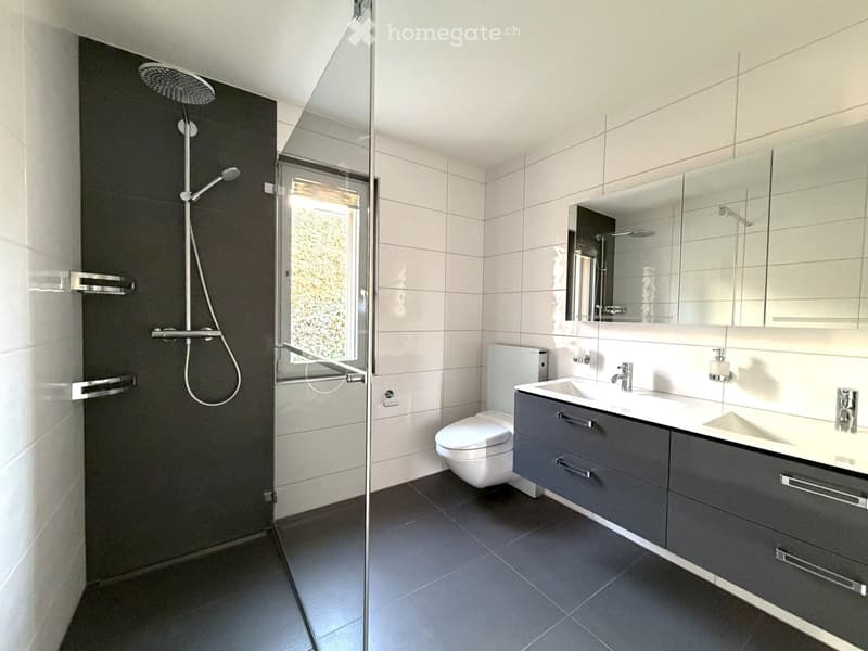 Modern bathroom with white tiles, glass walk-in shower, 2 white sinks, white toilet, mirrors, faucets, and showerhead