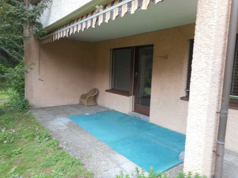 Balcony with a blue floor, a single chair, and a covered entrance to the building.
