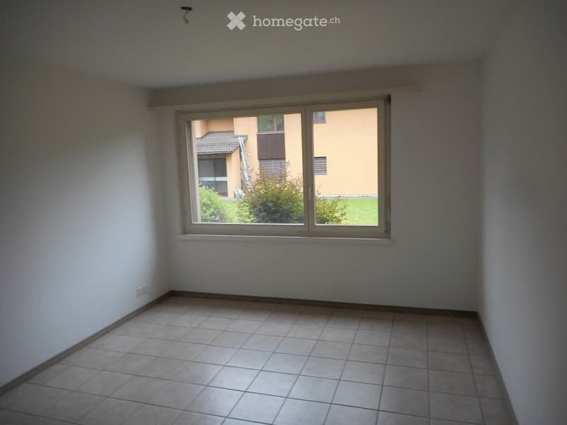 Empty room with tiled floor and large window showing a view of a building and greenery outside.