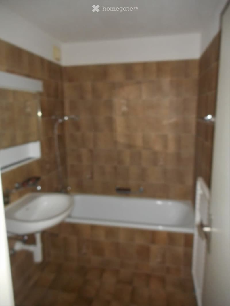 Bathroom with brown tiled walls and floor, a white bathtub, a sink, and a mirror above it.